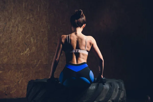 Mujer fitness volteando neumático de rueda en el gimnasio. Ajuste atleta femenina haciendo ejercicio con un neumático enorme. Vista trasera. Deportiva haciendo un entrenamiento de fuerza . —  Fotos de Stock