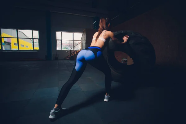 Γυμναστήριο γυναίκας flipping τροχός ελαστικών στο γυμναστήριο. Ταιριάζει αθλήτρια που εργάζονται έξω με μια τεράστια ρόδα. Πίσω όψη. Άσκησης και αθλήτρια που κάνει μια δύναμη. — Φωτογραφία Αρχείου
