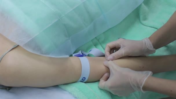 Медсестра, собирающая кровь из вены пациента, которая лежит на медицинской кровати в клинике, женщина проходит обследование крупным планом — стоковое видео