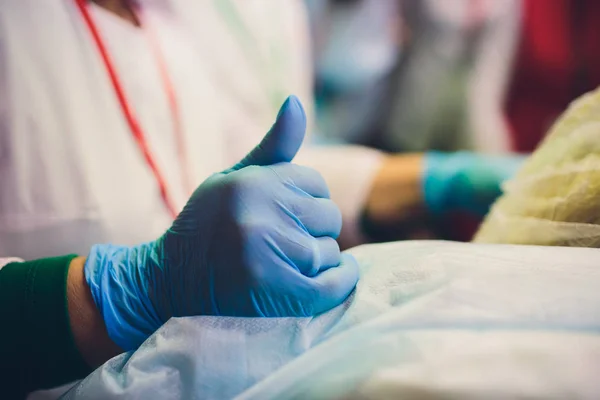 Primer plano de las manos de las médicas que se ponen guantes quirúrgicos esterilizados azules en la oficina. con el pulgar hacia arriba . — Foto de Stock