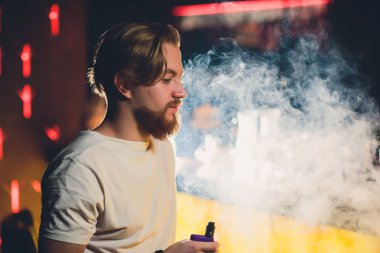 Bir fincan kahve, vaping ve bültenleri ile kafede oturmuş sakallı genç yakışıklı hipster adam Buhar bulutu.