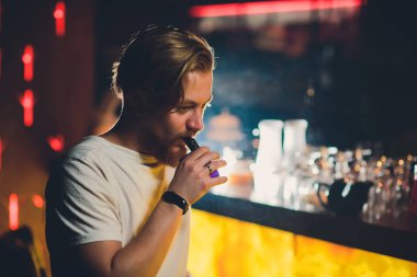 Bir fincan kahve, vaping ve bültenleri ile kafede oturmuş sakallı genç yakışıklı hipster adam Buhar bulutu.