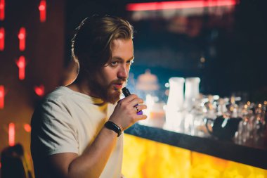 Bir fincan kahve, vaping ve bültenleri ile kafede oturmuş sakallı genç yakışıklı hipster adam Buhar bulutu.