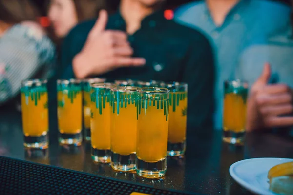 Many shot glasses with alcohol and citrus fruits juice.