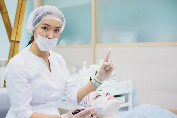 Il medico-cosmetologo fa una procedura di pulizia facciale ad ultrasuoni della pelle di una bella, giovane donna nel salone di bellezza, spa. Cosmetologia e cura della pelle professionale . — Foto Stock
