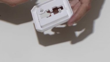 Hand cleaning a white home kitchen flat panel light switch with a white cotton cloth dust rag as part of regular housecleaning chores.