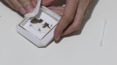 Hand cleaning a white home kitchen flat panel light switch with a white cotton cloth dust rag as part of regular housecleaning chores.
