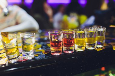 Bar tezgahında servis edilen sert alkollü içkilerin çeşitleri. Arka planda bulanık şişeler.