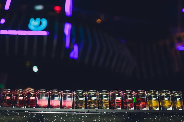 Variação de tiros alcoólicos duros servidos no balcão do bar. Frascos de borrão no fundo. — Fotografia de Stock