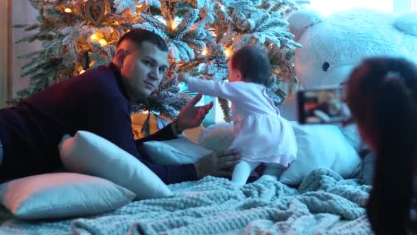Feliz família sorridente perto da árvore de Natal. mulher tira fotos no telefone de uma criança — Vídeo de Stock