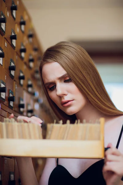 Mooi jong meisje met donkere sluik haar vak en zoekt gegevens geopend in de archiefkast in de bibliotheek — Stockfoto