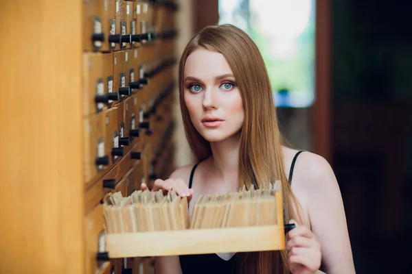 Hermosa joven con cabello liso oscuro abre caja y busca datos en el gabinete de archivos en la biblioteca — Foto de Stock