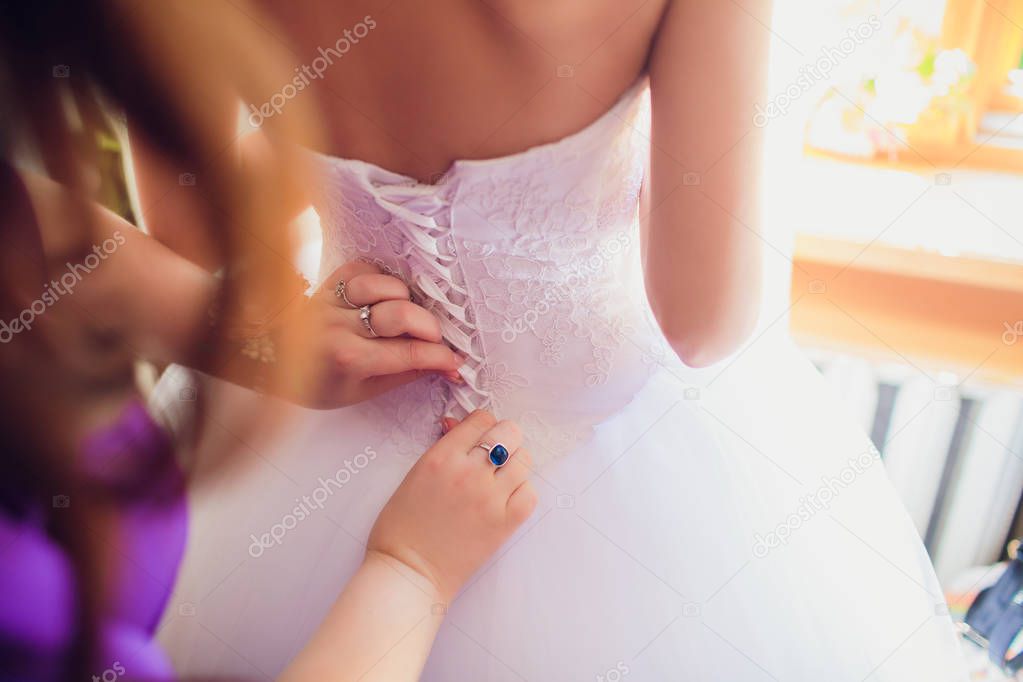 Bridesmaid is helping bride to dress