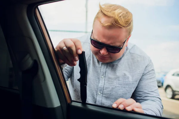 An offender in black clothes and mask is trying to steal car in parking lot. Stop criminality. — Stock Photo, Image