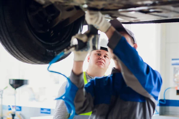 Mladí mechanik upínání kotouče pod auto v provozu — Stock fotografie