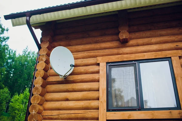 Antenne satellite sur le mur de la maison. L'antenne est blanche. La maison est faite de poutre en bois de couleur marron. Gros plan. Personne sur la photo . — Photo