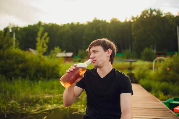 Закройте человека, пьющего пиво из стекла на открытом воздухе возле бассейна. Концепция алкоголя и досуга. на заднем плане деревянного дома — стоковое фото