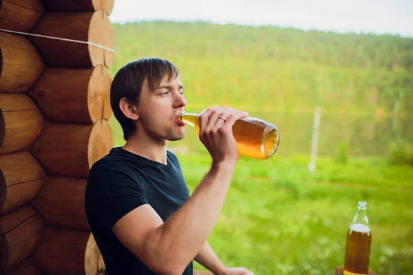 Закройте человека, пьющего пиво из стекла на открытом воздухе возле бассейна. Концепция алкоголя и досуга. на заднем плане деревянного дома — стоковое фото