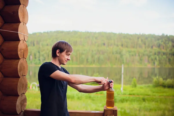 Close up man drinking beer from glass at open air near the pool. Alcohol and leisure concept. on the background of a wooden house