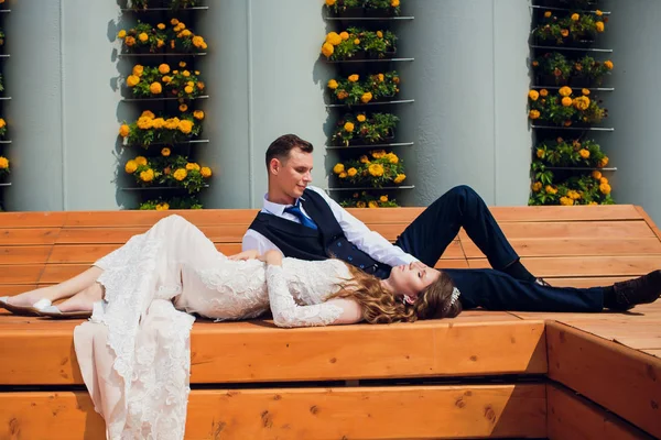 Dva milenci sedět na lavičce, novomanželé se krčil v ostatních zbraní během svatební fotografie střílet, nevěsta v bílých šatech a ženich v krásný oblek, do důchodu v parku. — Stock fotografie