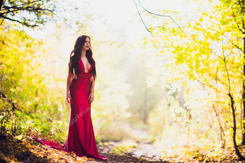 Woman in a long red dress alone in forest. Fabulous and mysterious image of a girl in a dark forest in the evening sun. Sunset, Princess got lost.