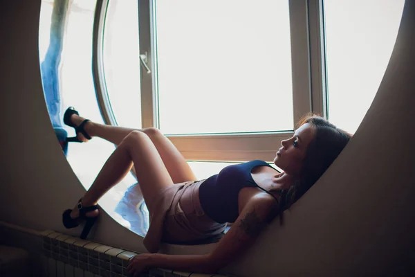 Ruha szép lány fekszik a kerek ablak nyílászáró — Stock Fotó