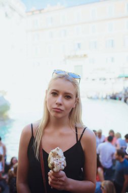 Ice cream, young beautiful blond girl in a bright outfit gets pleasure from ice cream. Tastes like a yellow Eskimo. Having fun. Indoor. White background. clipart