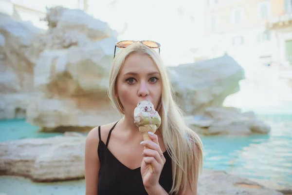 Eis, junge schöne blonde Mädchen in einem hellen Outfit bekommt Freude an Eis. schmeckt wie ein gelber Eskimo. Spaß haben. Innenraum. weißer Hintergrund. — Stockfoto
