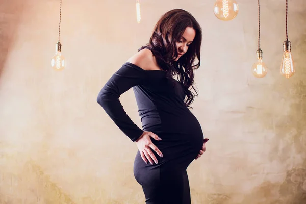 Piękna młoda kobieta w ciąży w czarnej sukni pozowanie w hali. — Zdjęcie stockowe