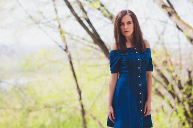 Doğa orman arka planda kamera önünde poz mavi elbiseli güzel genç kadın.