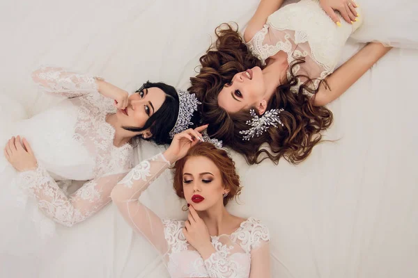 Vista superior de la novia con amigas acostadas en la cama y sonriendo. Tres mujeres jóvenes tumbadas en la cama en casa . — Foto de Stock