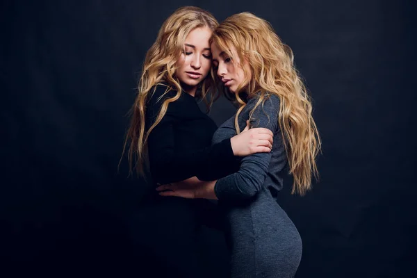 Deux belles femmes en robe de nuit noire posant isolées sur un fond gris blanc. Jolie brune amies jumelles s'amusant à boire des cocktails. Chanter et danser. Humeur festive. À l'intérieur — Photo