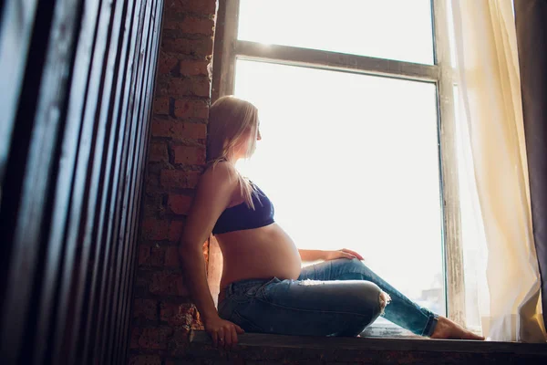 Fiatal szép terhes nő ül otthon ablakpárkányon. — Stock Fotó