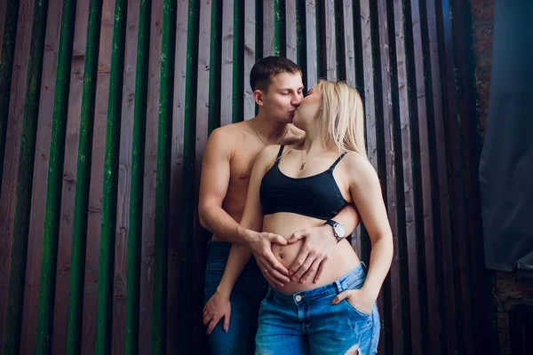 Gravida par i kärlek står nära trävägg, skrattar och väntar på sina barn. Väntar på ett mirakel, lyckliga föräldrar, Familj. — Stockfoto