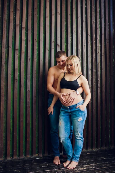 Casal grávida apaixonado de pé perto da parede de madeira, rindo e esperando por seu bebê. Esperando por um milagre, pais felizes, família . — Fotografia de Stock