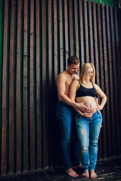 Těhotné ženy v stojící u dřevěné stěny, smáli se a čeká na své dítě. Čekání na zázrak, šťastné rodiče, rodina. — Stock fotografie