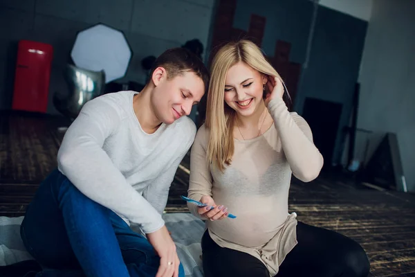 Těhotná rodina s penězi a baby oblečení sedět na pohovce domu. Rodinný rozpočet. — Stock fotografie