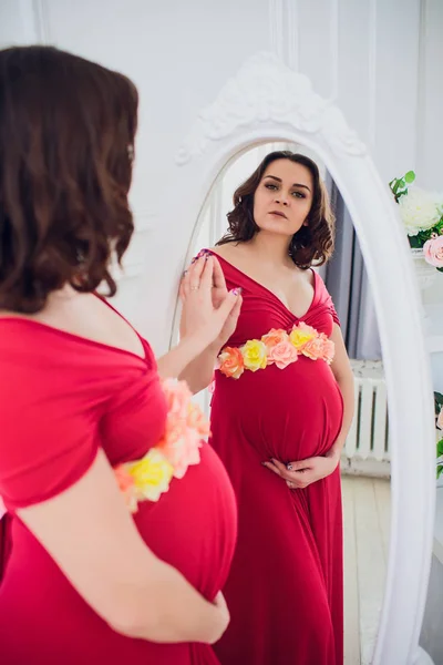 Bella donna incinta guardando nello specchio nella stanza della luce — Foto Stock