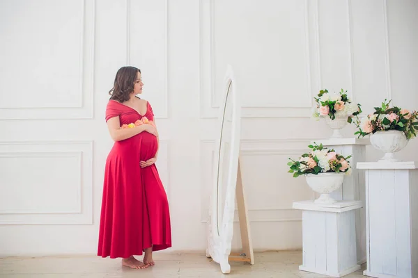 Bella donna incinta guardando nello specchio nella stanza della luce — Foto Stock