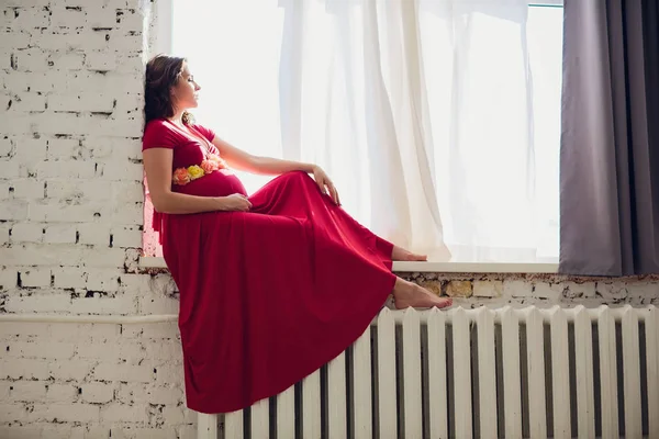 Terhes nő egy piros ruhás feküdt az ablak — Stock Fotó
