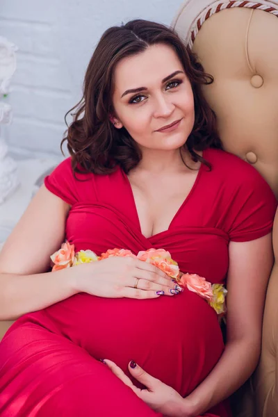 Těhotná žena v červených šatech ležela na pohovce — Stock fotografie