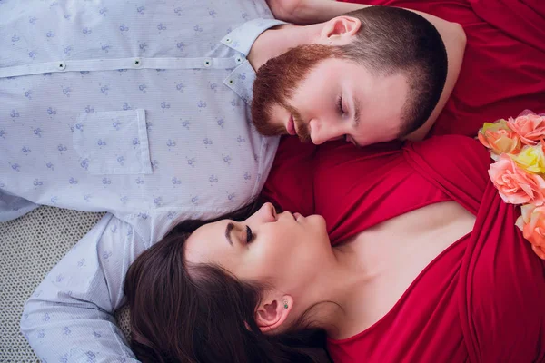 Een mooie zwangere vrouw in zwarte ondergoed ligt op een grijze sluier. Het bed is gedecoreerd met verse bloemen. Het meisje heeft blonde haren, ze glimlacht. Van bovenaf bekijken. — Stockfoto