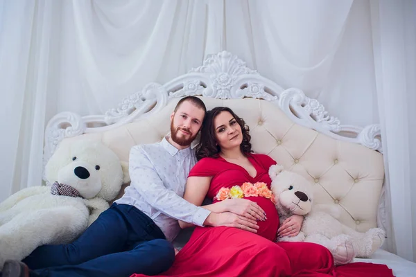 Junge Familie bereitet sich darauf vor, Eltern zu werden. Mann umarmt seine schwangere Frau zu Hause sanft auf der Couch. Konzept der Mutterschaft und Vaterschaft. — Stockfoto