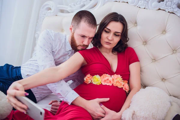 Manžel a těhotnou manželku udělat selfie sedí na gauči. Milují jeden druhého. Oni jsou doma. — Stock fotografie