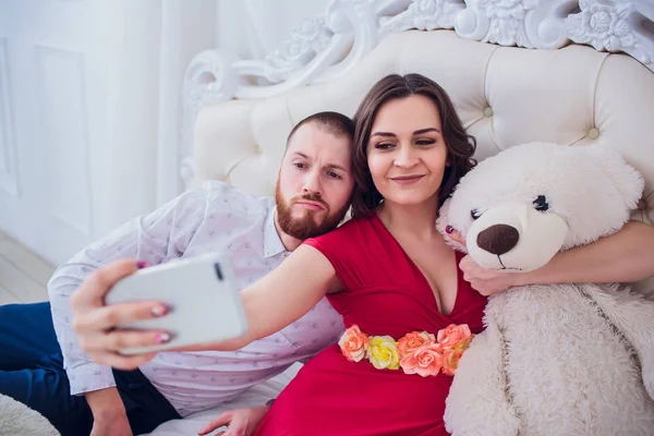 Ein Mann und eine schwangere Frau machen ein Selfie auf der Couch. Sie lieben einander. Sie sind zu Hause. — Stockfoto
