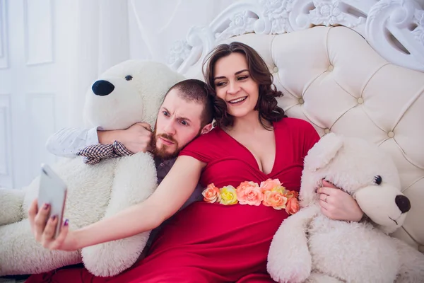 Un mari et une femme enceinte font du selfie assis sur le canapé. Ils s'aiment. Ils sont chez eux. . — Photo