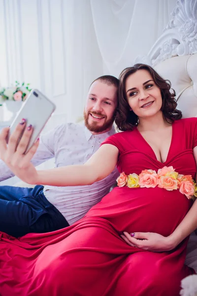 Manžel a těhotnou manželku udělat selfie sedí na gauči. Milují jeden druhého. Oni jsou doma. — Stock fotografie