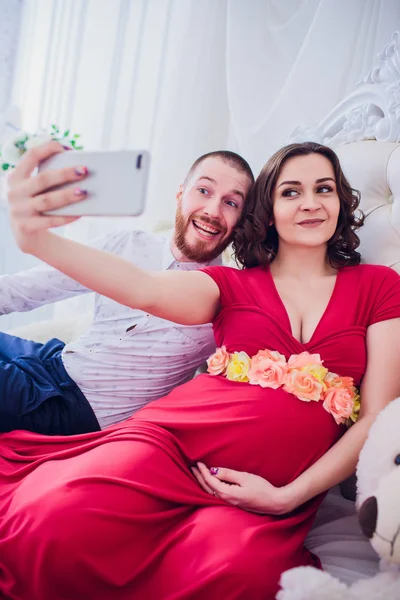 Manžel a těhotnou manželku udělat selfie sedí na gauči. Milují jeden druhého. Oni jsou doma. — Stock fotografie