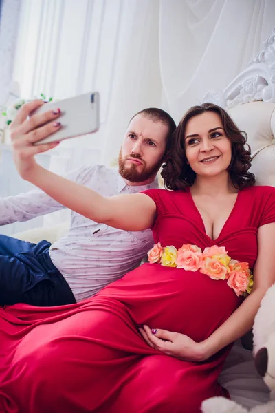 Manžel a těhotnou manželku udělat selfie sedí na gauči. Milují jeden druhého. Oni jsou doma. — Stock fotografie