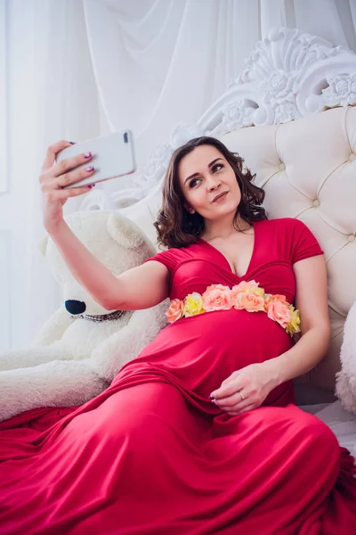 Felice donna incinta sorridente seduta sull'erba e fa autoritratto su smartphone. la donna incinta fa selfie . — Foto Stock